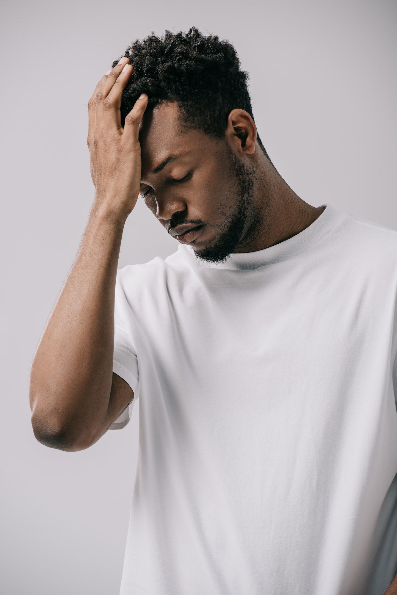 sad african american man touching hair isolated on grey